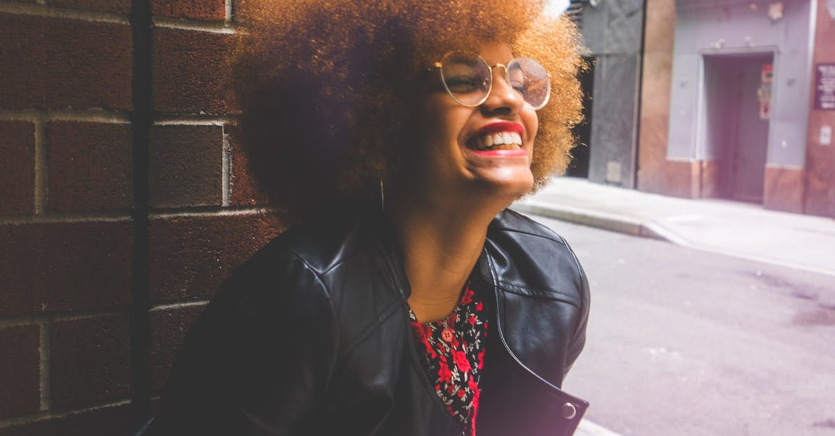 Joyful woman with afro hair and glasses smiles brightly outdoors in urban setting.