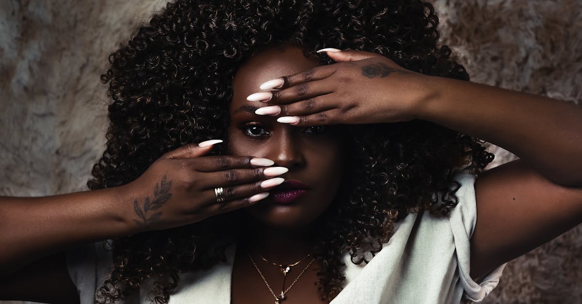 A powerful portrait of a woman with curly afro hair and tattoos covering her face with hands.