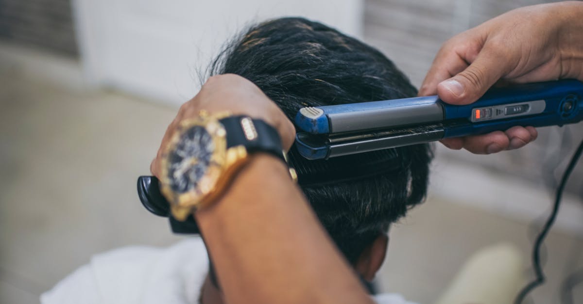 Close-up of a hairdresser styling a client's hair using a straightener in a barbershop.