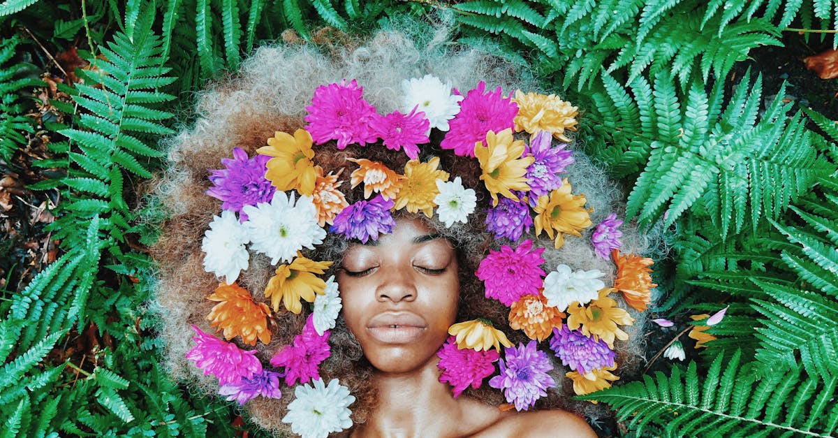A serene portrait of a woman with flowers in her afro, surrounded by lush green ferns.