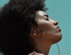 From below side view of young reflective ethnic female model with big earrings and closed eyes under blue sky