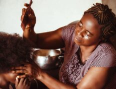 A loving mother combs her son's afro hair at their home in Abuja, Nigeria, showcasing family care and connection.