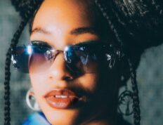 Fashionable woman in afro braids and sunglasses, showcasing urban style outdoors.
