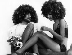 Creative, black and white portrait of two individuals with afro hairstyles sitting on the floor.
