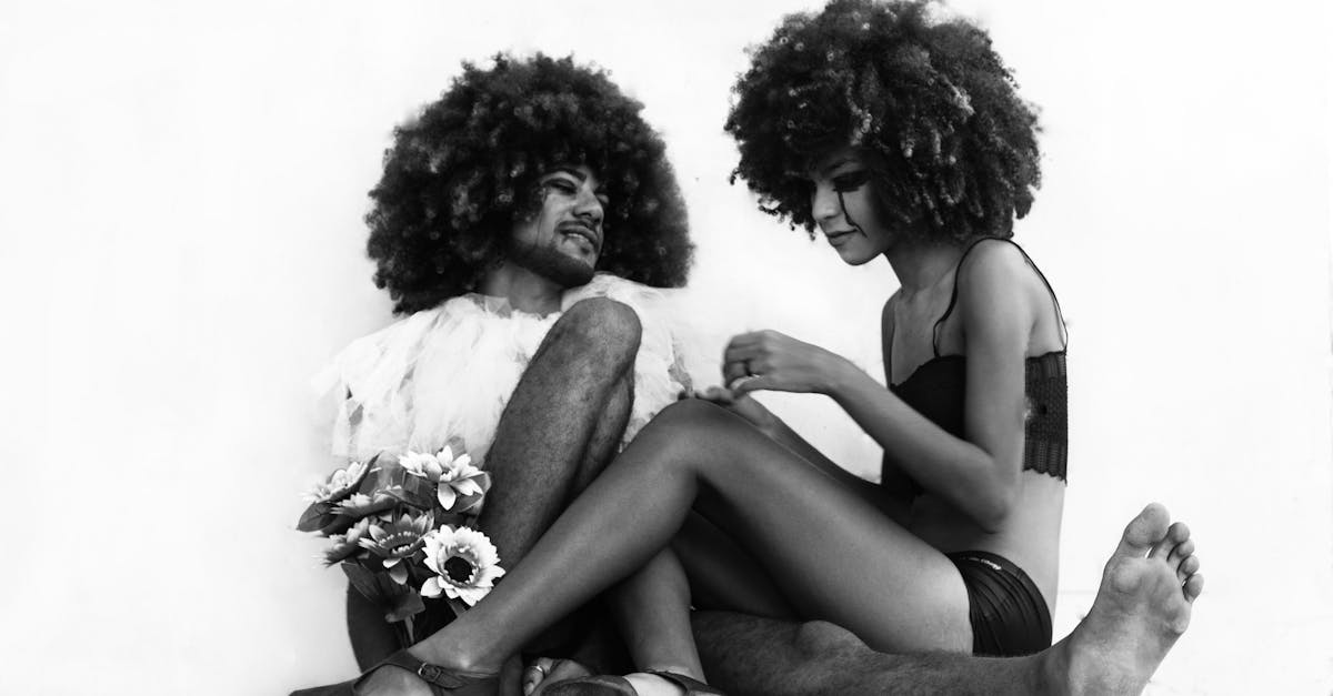 Creative, black and white portrait of two individuals with afro hairstyles sitting on the floor.