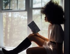 A woman enjoys a peaceful reading session by a window, bathed in natural light.