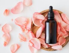 Top view of empty brown bottle for skin care product placed on wooden plate with fresh pink rose petals on white background isolated